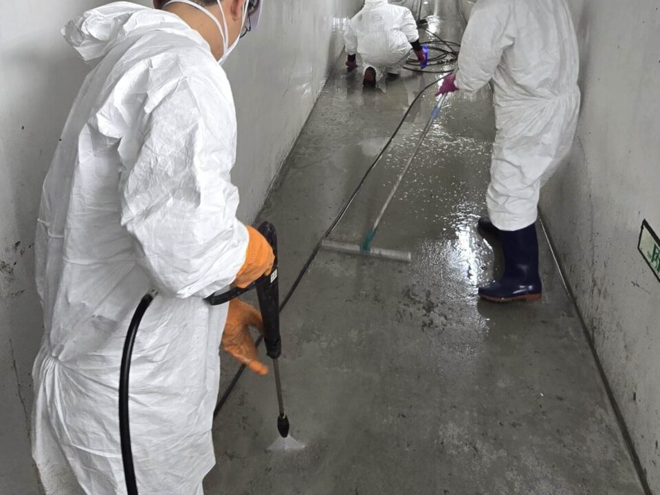 방진복과 보호구를 착용한 특수청소 작업자들이 지하 통로에서 고압세척과 소독 작업을 하는 모습